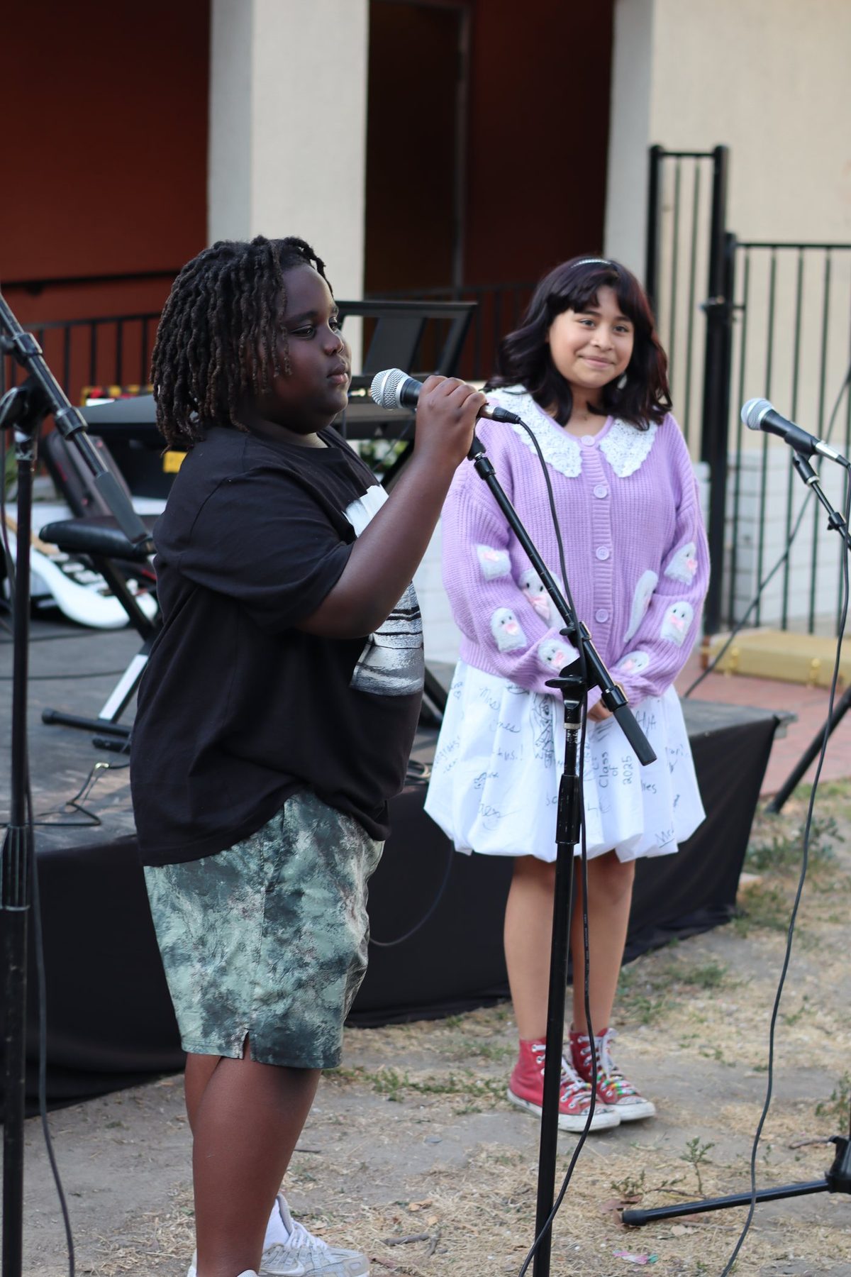 A mentor beside a young student singing at the microphone
